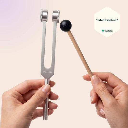 OM 136.1 Hz tuning fork and mallet held by hands with Trustpilot rating on a beige background