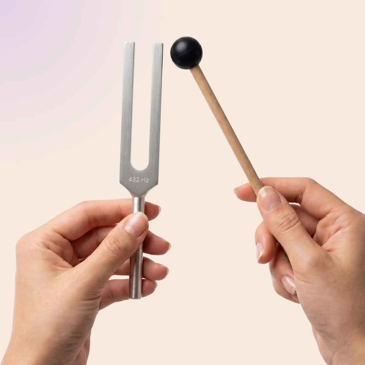 432 Hz tuning fork with a mallet held by hands against a light pink background
