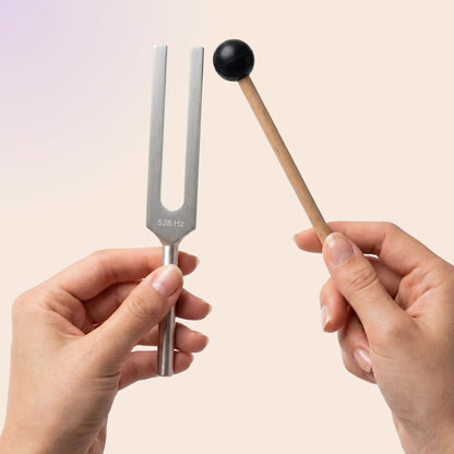 528 Hz tuning fork held by a hand with a mallet, on a beige background
